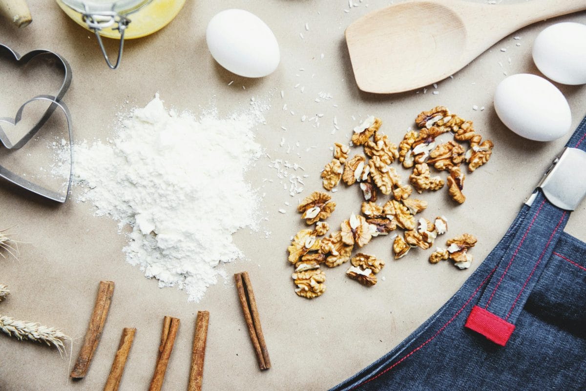 Overhead view of baking ingredients including eggs, flour, walnuts, and cinnamon sticks on a table.
