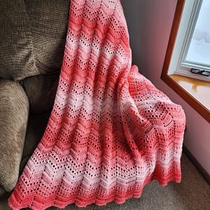 Full sized Ripple Stripe afghan in an ombre coral color displayed on recliner