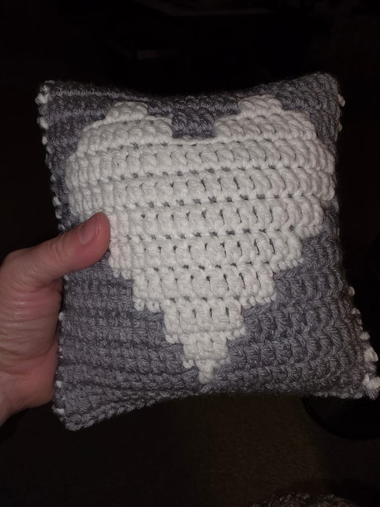 small pillow made from two heart blocks whip stitched together - both sides have white hearts with gray background