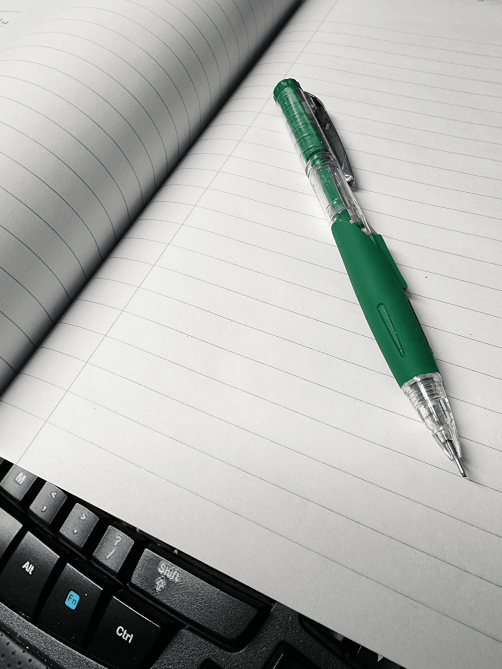 Notebook laying on keyboard with pencil on top.